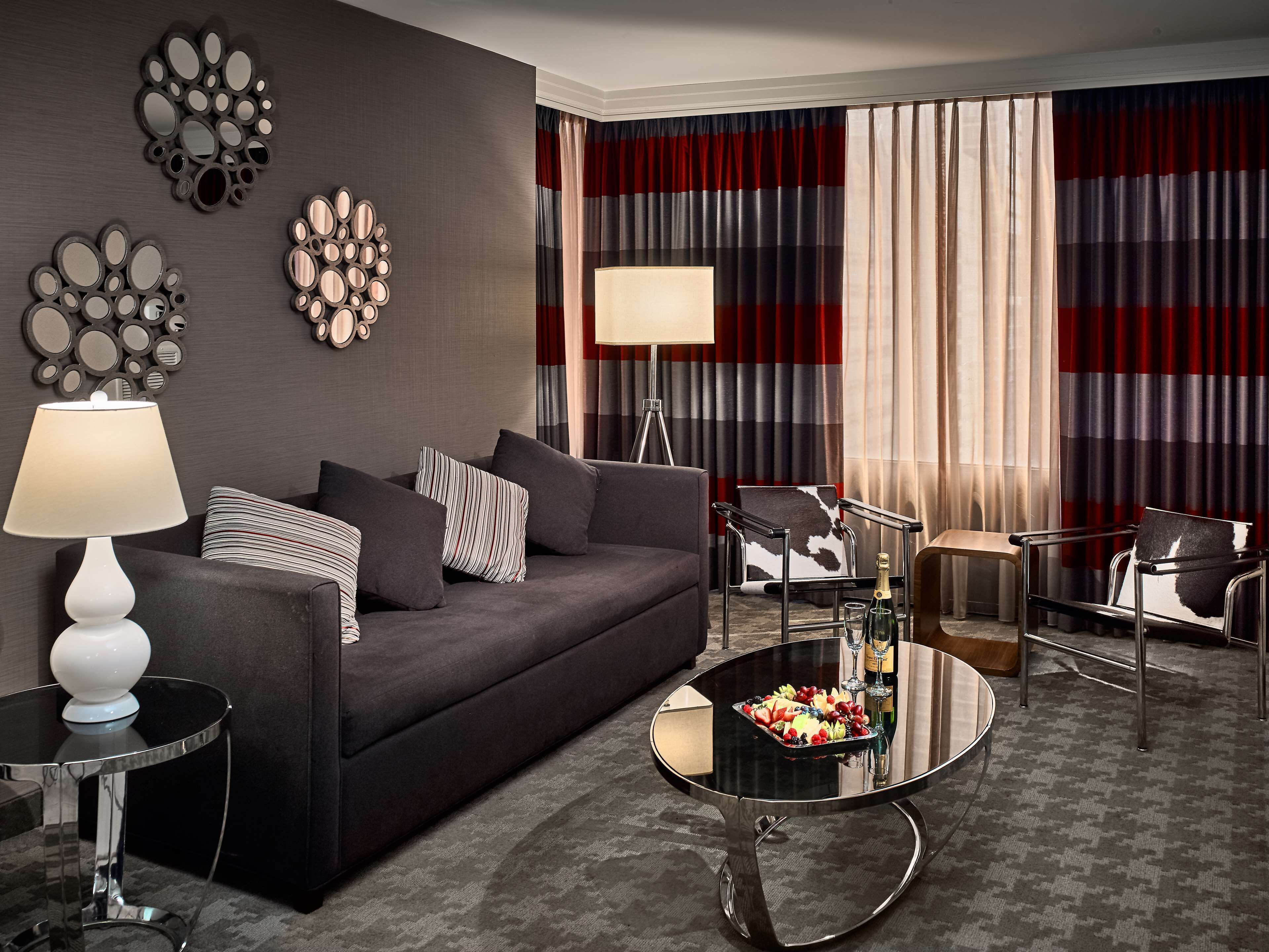 A modern living room with a dark grey sofa, striped pillows, a glass coffee table with fruit, and a red and grey striped curtain backdrop.