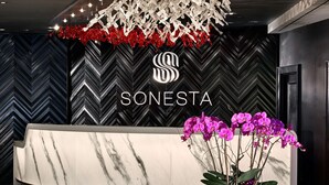 A reception area with a modern design, featuring a marble reception desk, a logo above the desk, and a glass table with a decorative metal sculpture.