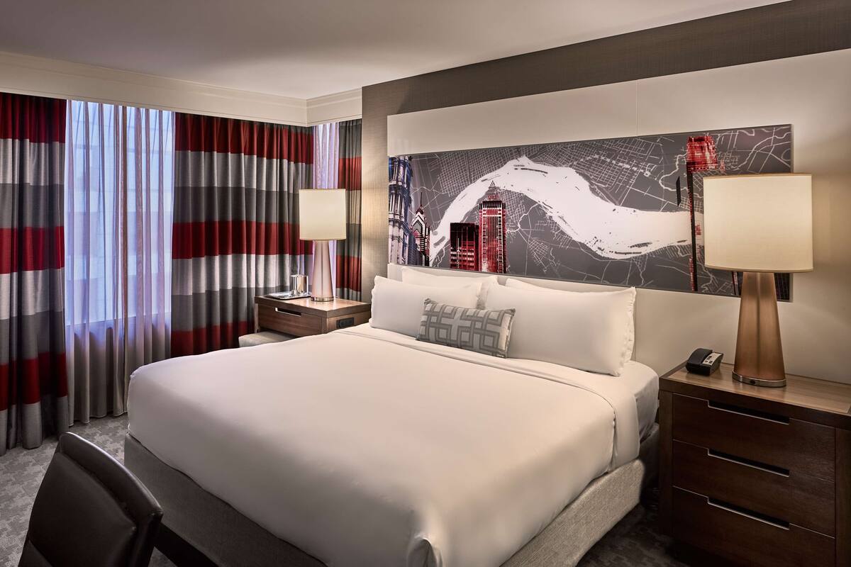 Une chambre d’hôtel avec un grand lit, deux tables de chevet, une petite table, un bureau et une chaise.