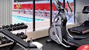 A gym with exercise equipment, a bench, dumbbells, a water bottle, and a view of a pool through large windows.