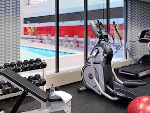 A gym with exercise equipment, a bench, dumbbells, a water bottle, and a view of a pool through large windows.