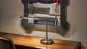 A modern hotel room with a large mirror, a wooden desk, a chair, and a coffee maker.