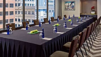 A conference room with a long table, chairs, and a city view through large windows.