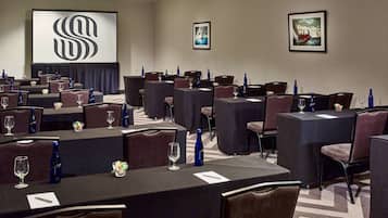 A conference room with multiple tables, chairs, and a large screen displaying a logo.