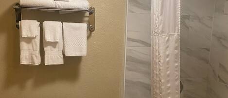 A bathroom with a toilet, a towel rack with folded towels, and a shower curtain.