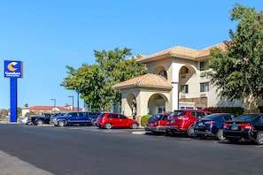 A Comfort Inn & Suites with a parking lot filled with cars, a clear blue sky, and a building with a tiled roof and arched windows.