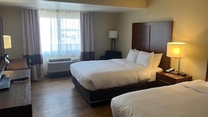 Ein Hotelzimmer mit zwei Betten, einem Schreibtisch, einem Stuhl, einer Lampe und einem Fenster mit Vorhängen.