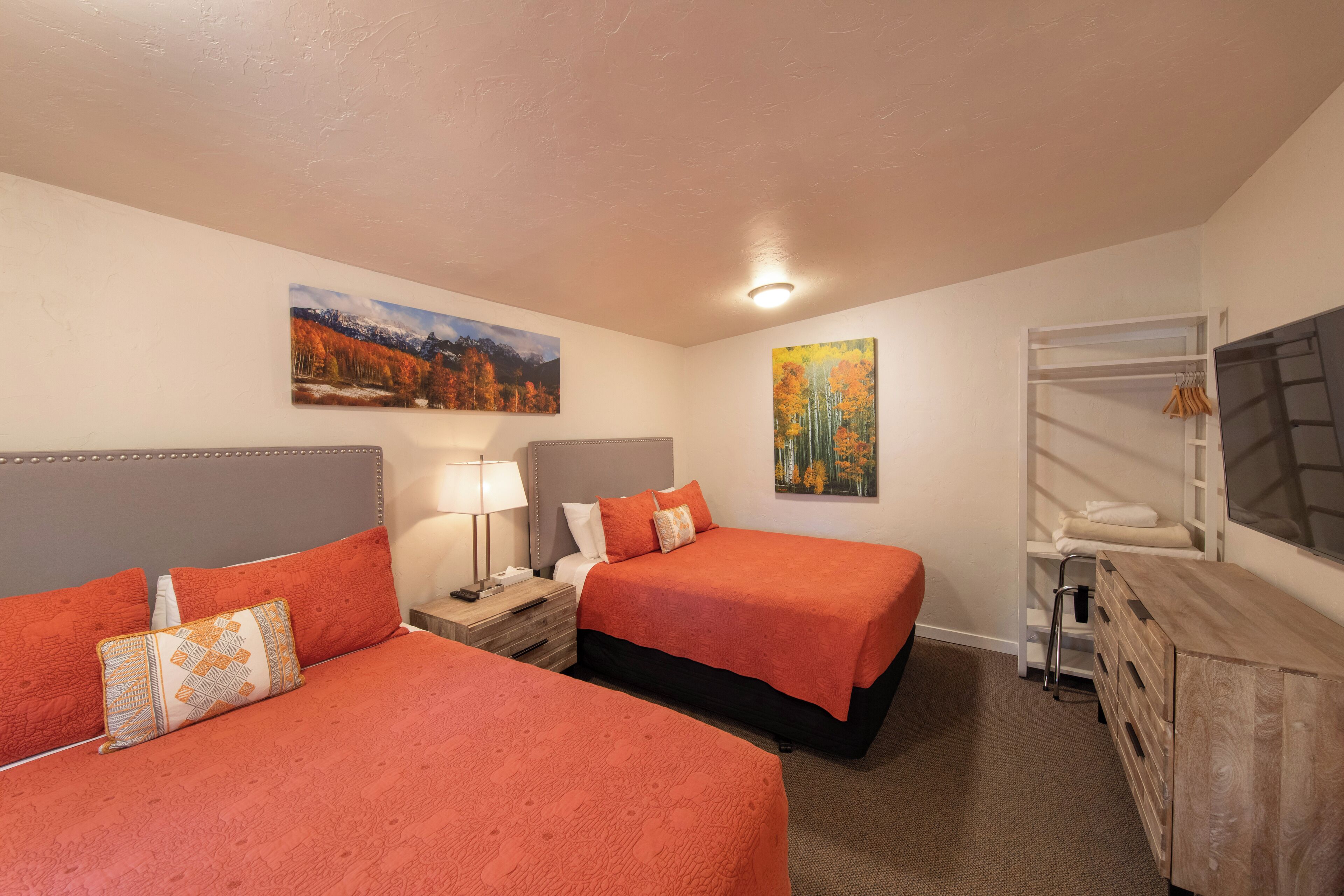 A hotel room with two beds, a wardrobe, a desk, and a painting on the wall.