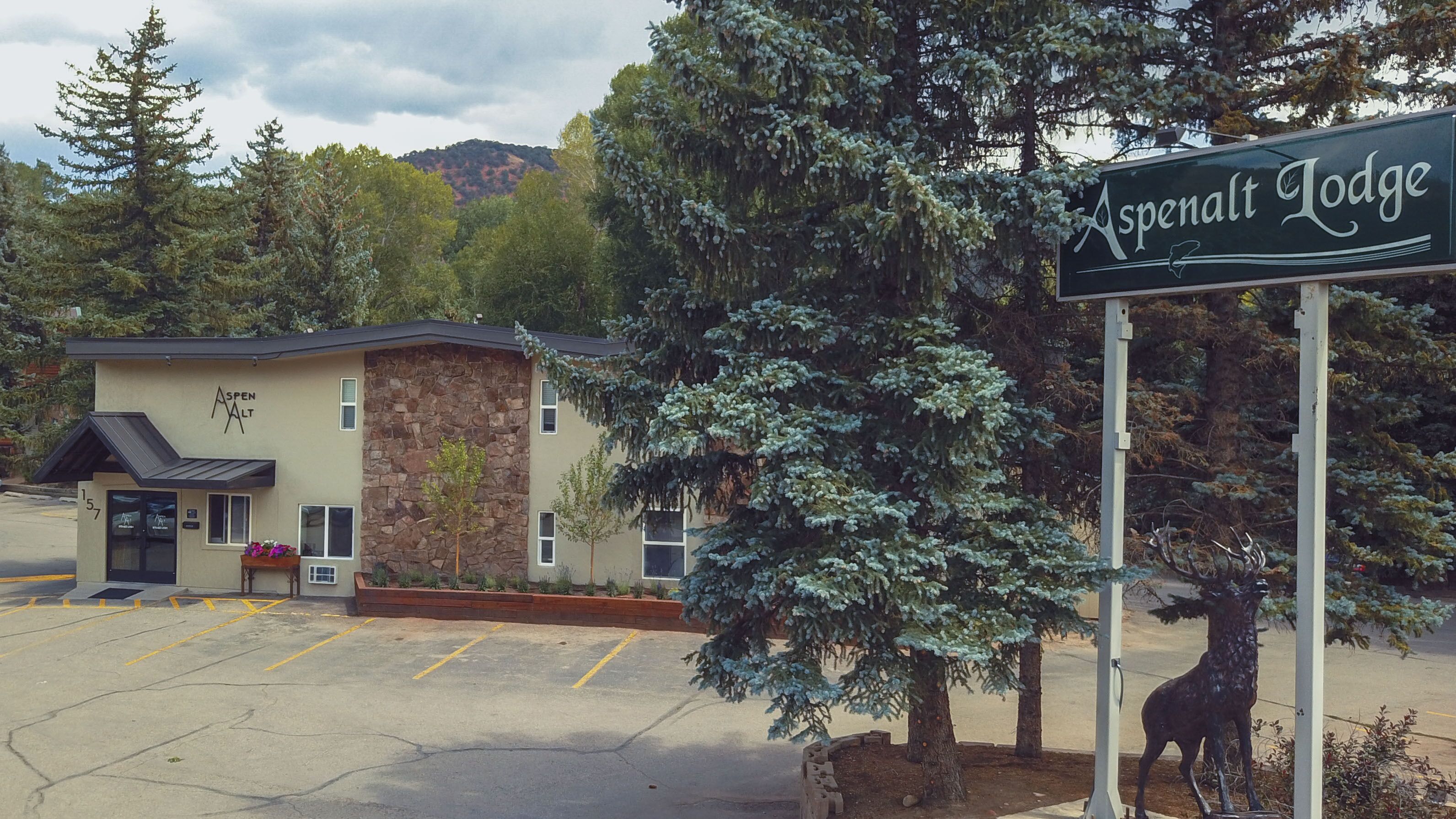 Aspen Lodge with a stone facade, a parking lot, and a mountain backdrop.