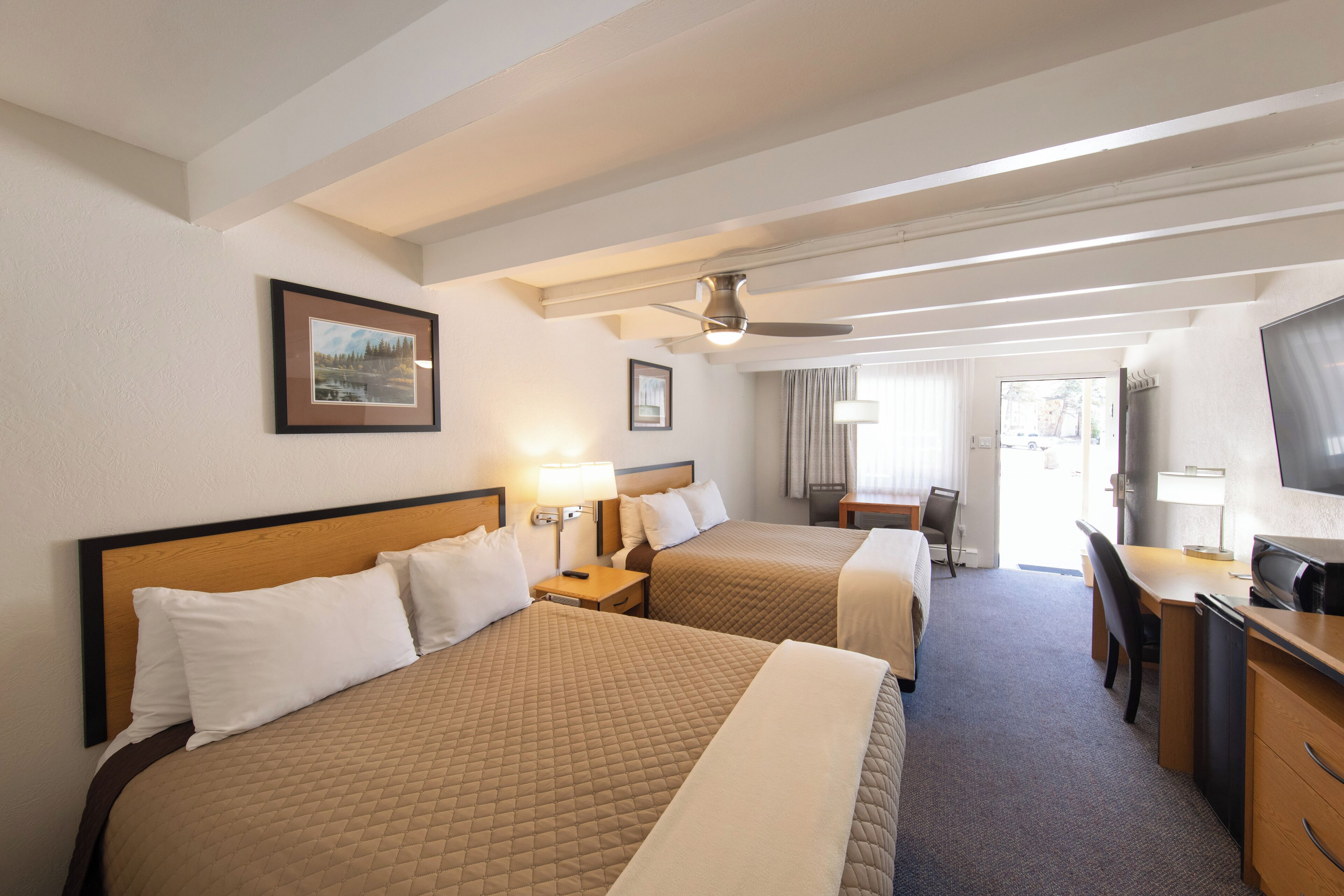 Une chambre d’hôtel avec deux lits, un bureau, une chaise, une télévision et un ventilateur de plafond.