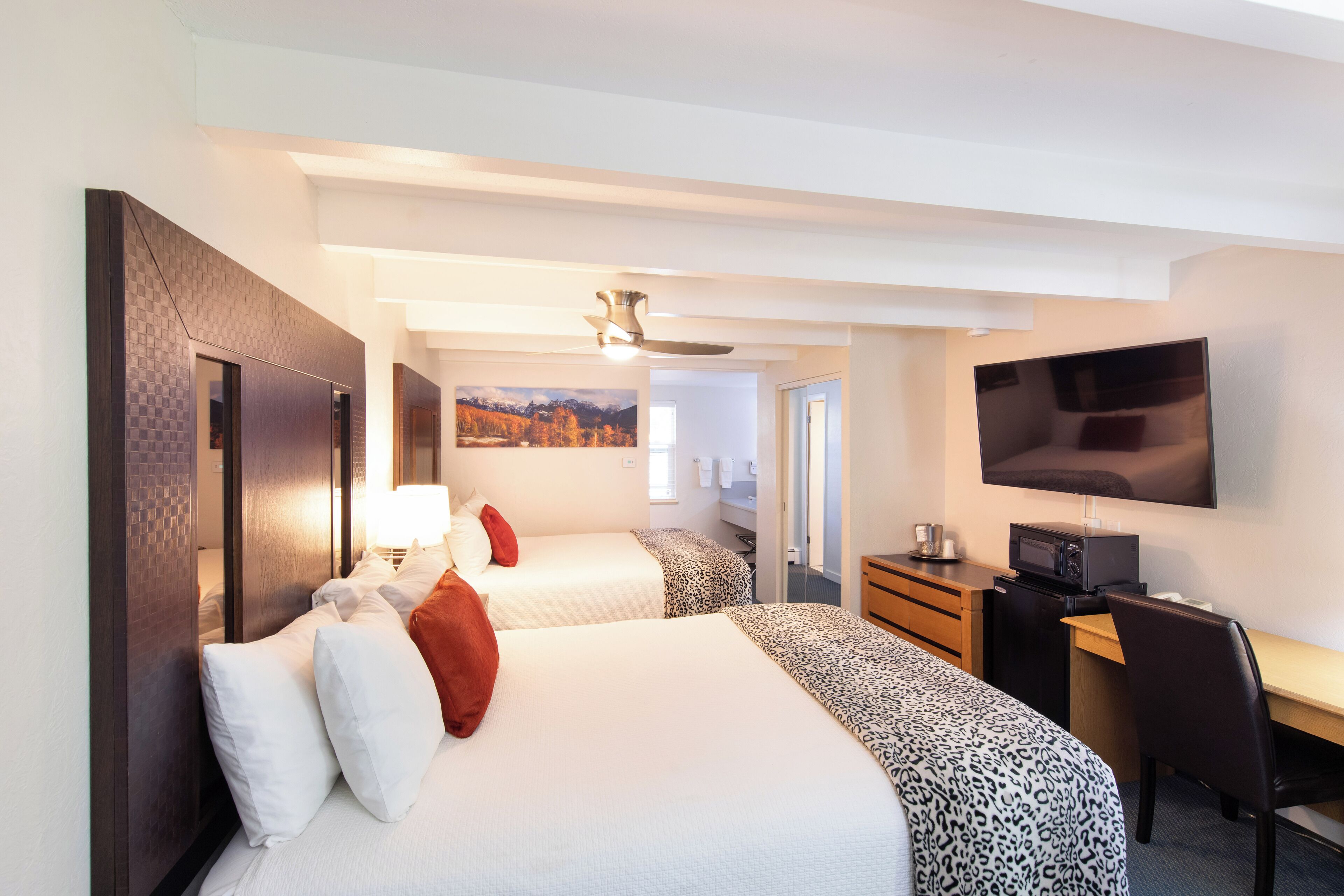 A hotel room with two beds, a desk, a TV, and a ceiling fan.
