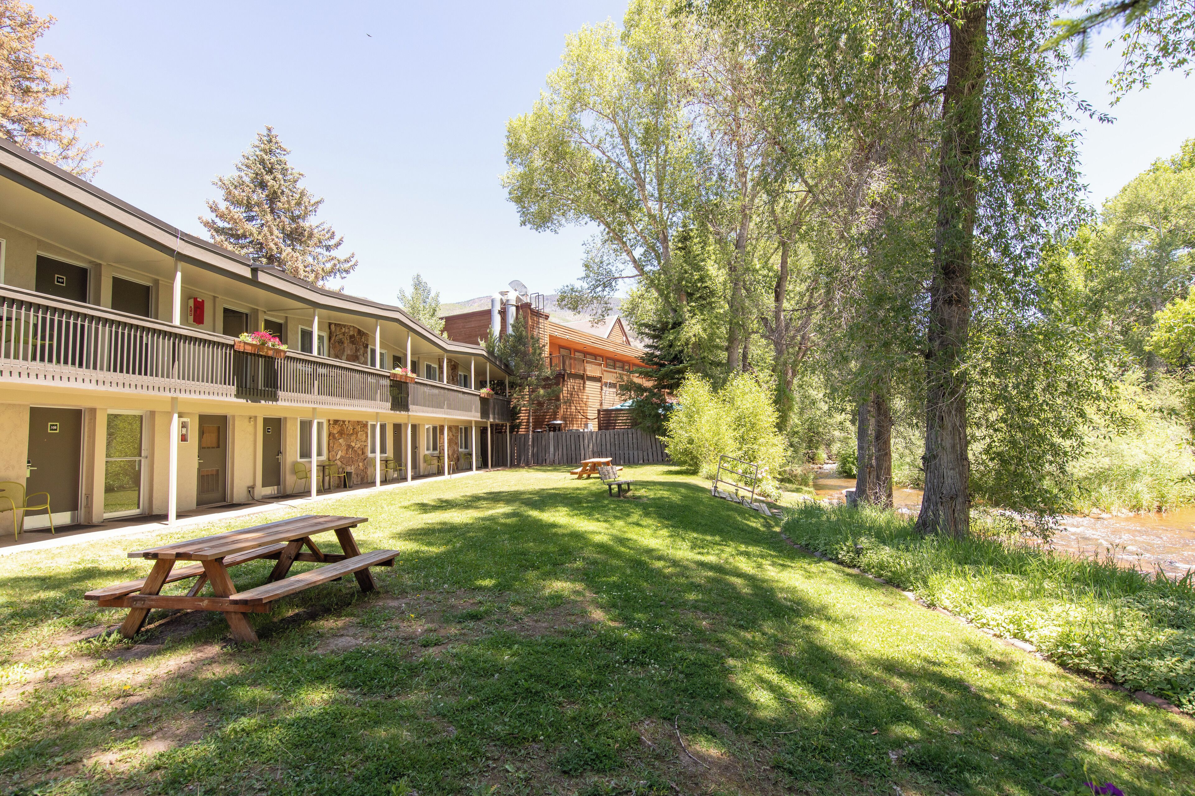 A multi-story building with a covered outdoor area, picnic tables, and a small stream.