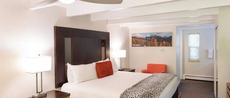 A hotel room with a bed, nightstands, a desk, a chair, a painting, and a door.