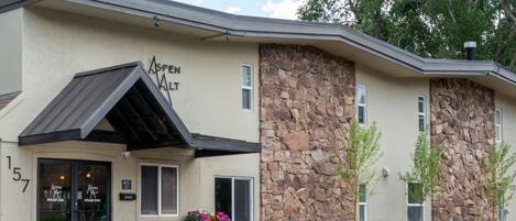 A building with a stone facade, a black awning, and a flower planter outside the entrance.