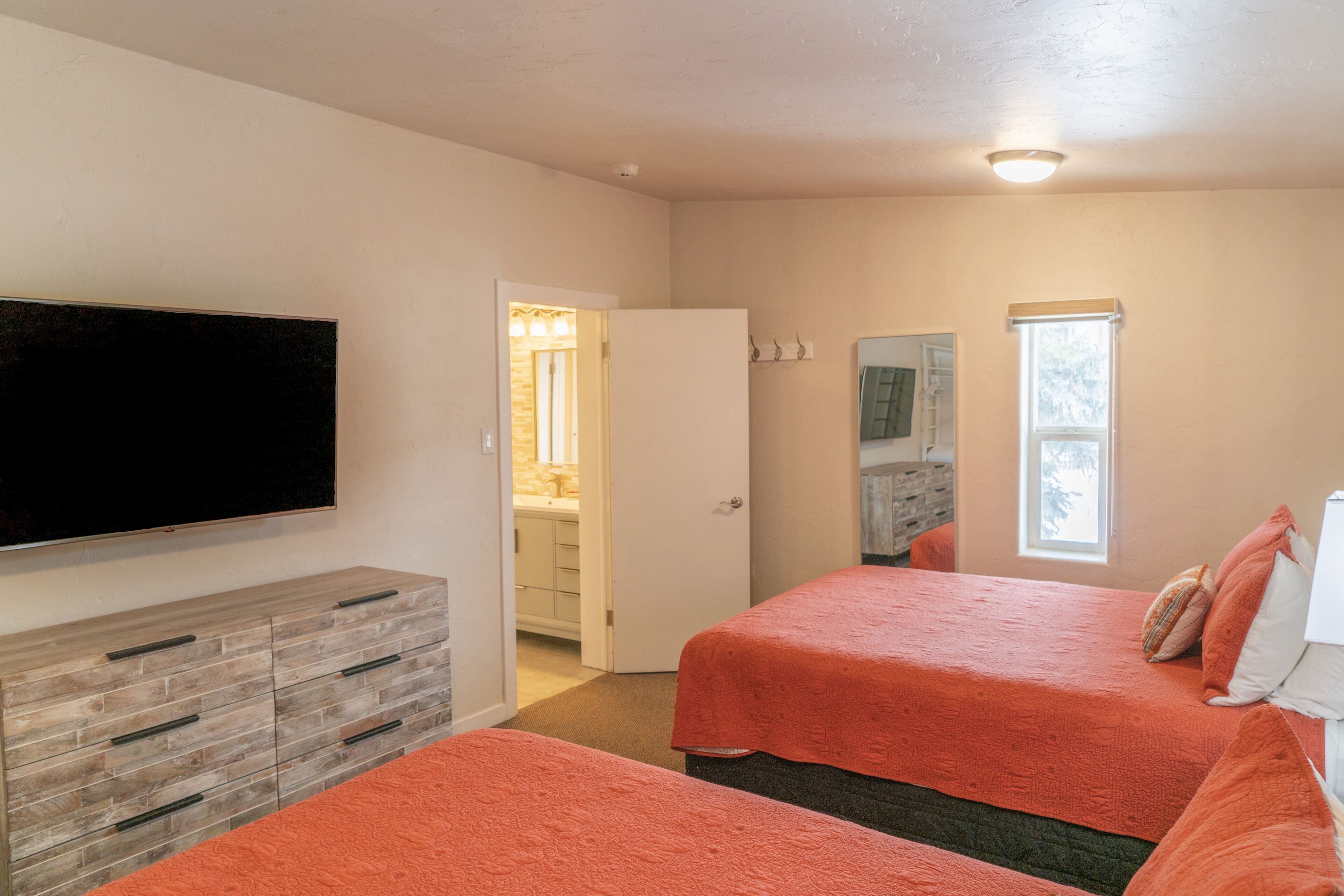 A bedroom with two beds, a TV, a dresser, and a bathroom visible through an open door.