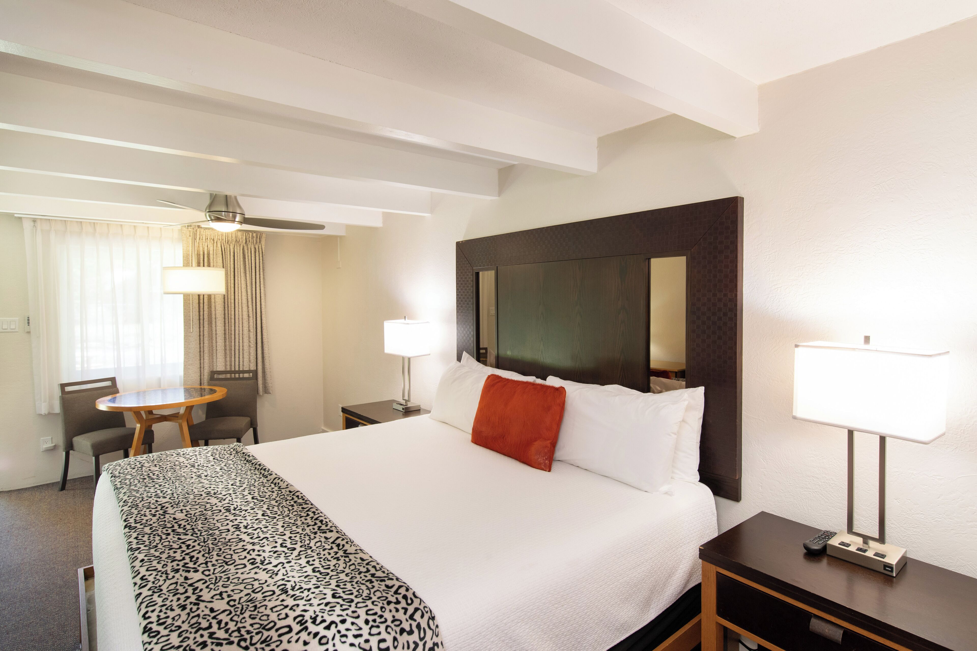 A hotel room with a large bed, a desk with a lamp, a chair, and a window with curtains.