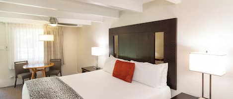 A hotel room with a large bed, a desk with a lamp, a chair, and a window with curtains.
