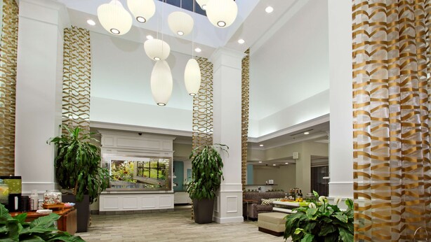 Um hall amplo com teto alto, luminárias pendentes modernas e grandes vasos de plantas.