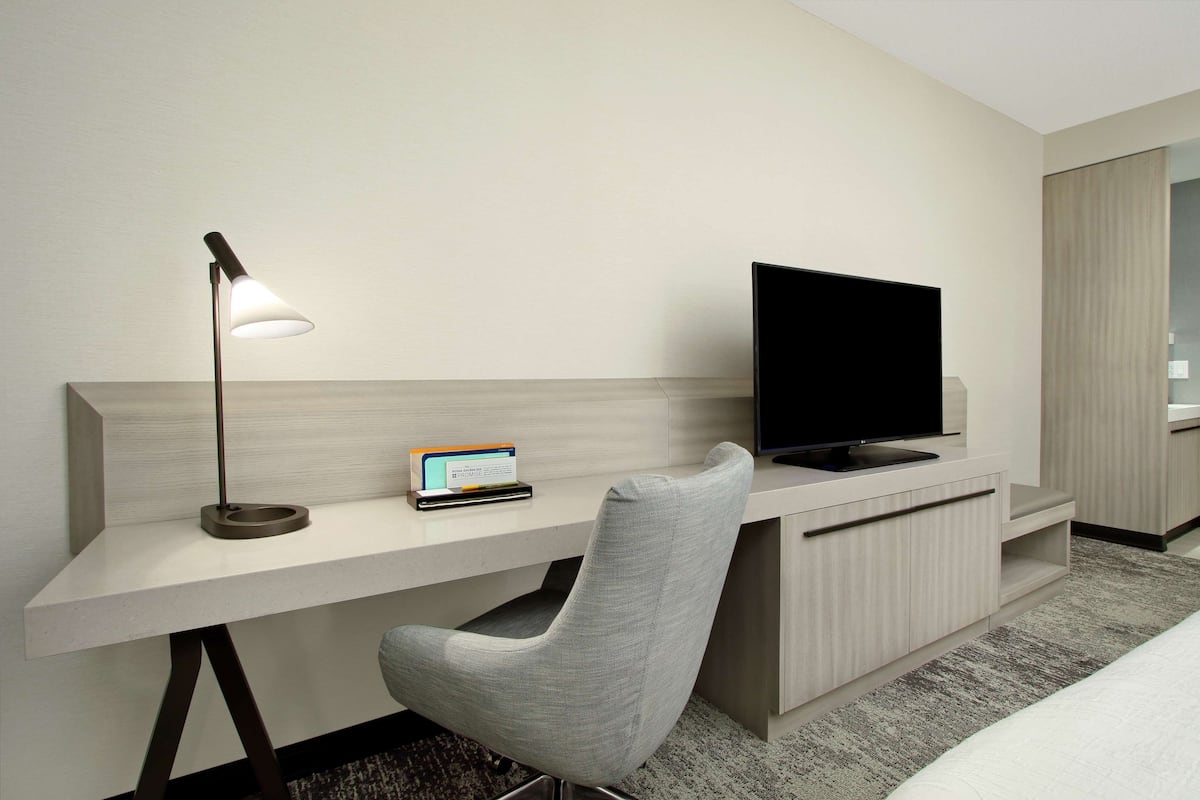 A modern hotel room with a desk, a television, a lamp, and a chair.