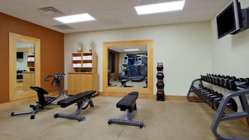 Un gimnasio con equipo de ejercicio, un espejo y un televisor en la pared.
