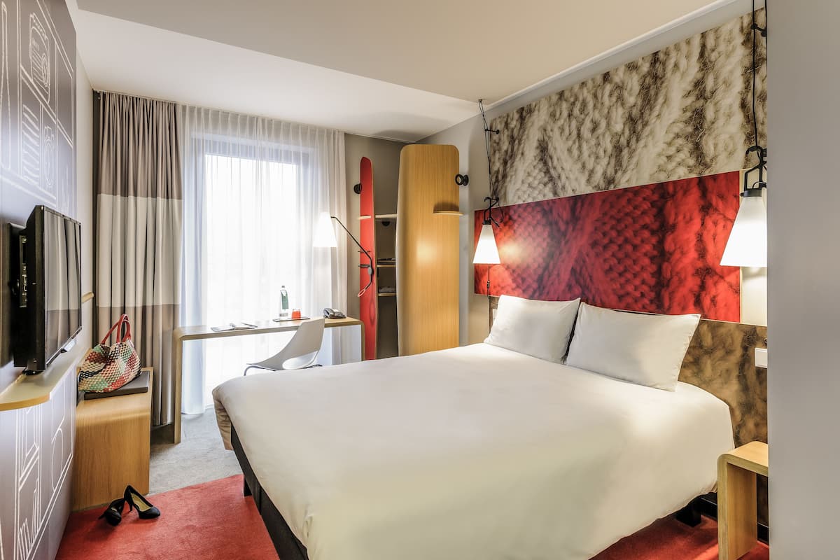 Ein Hotelzimmer mit einem großen Bett, einem Schreibtisch mit Stuhl, einem Fernseher und einem Kleiderschrank.