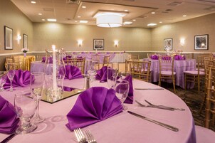 Un salón de banquetes con mesas redondas, manteles morados y sillas doradas.