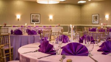 Une salle de banquet avec des tables rondes dressées pour le repas, chacune recouverte d’une nappe violette, agrémentée de couverts en argent et de verres.