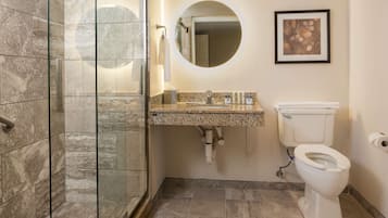 A bathroom with a glass-enclosed shower, a granite countertop sink, a toilet, and a framed picture on the wall.