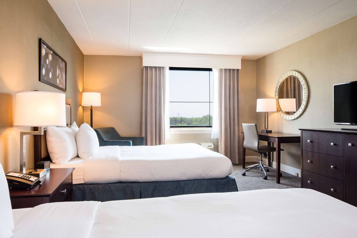 A hotel room with a large bed, two bedside tables with lamps, a desk with a chair, a dresser, and a television.