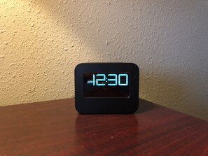 Reloj digital mostrando las 12:30 PM sobre una superficie negra frente a una pared con textura.