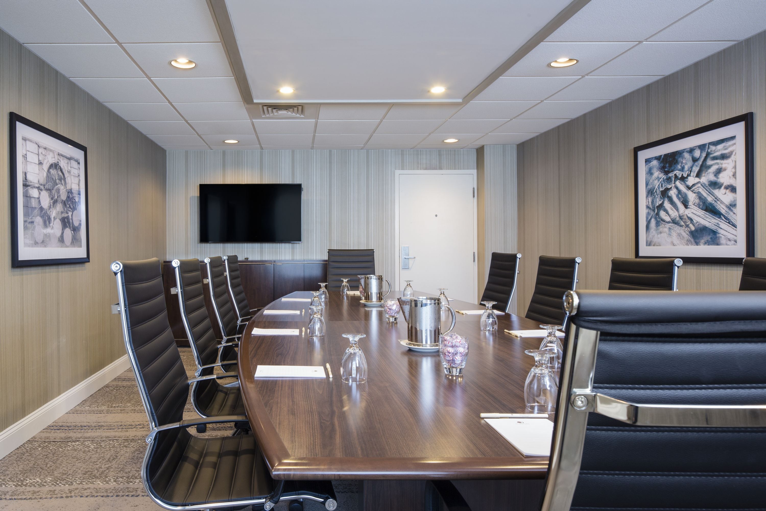 Ein Konferenzraum mit langem Tisch, schwarzen Ledersesseln, einem Flachbildfernseher und gerahmten Kunstwerken an den Wänden.