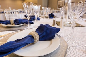 Una mesa dispuesta con platos blancos, servilletas azules y copas de vidrio.