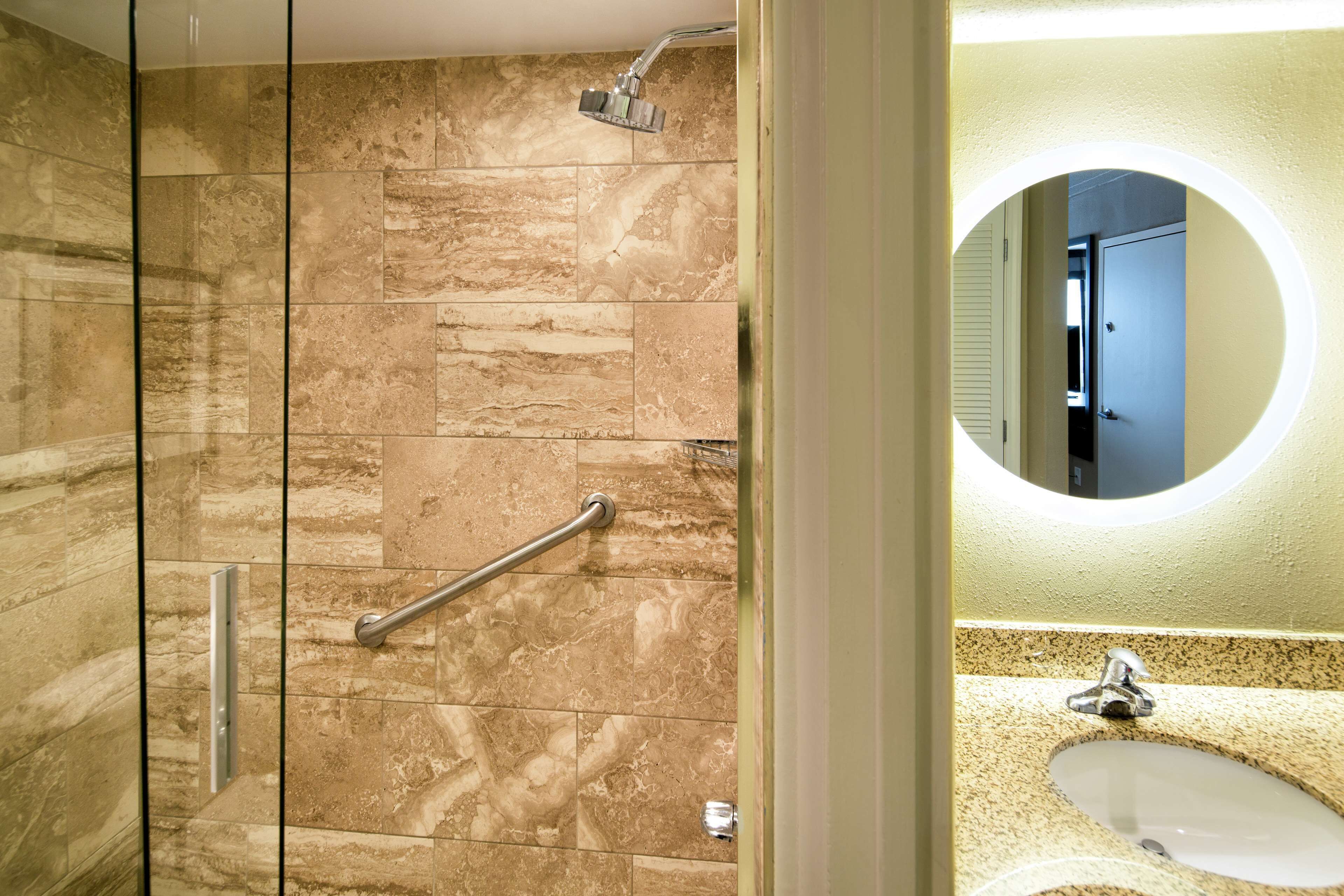 A bathroom with a shower, a handrail, a sink, and a mirror.