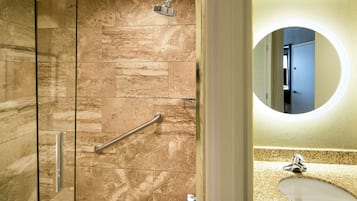 A bathroom with a shower, a handrail, a sink, and a mirror.