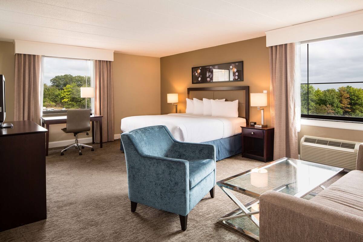 A hotel room with a bed, a desk, a chair, and a glass coffee table.