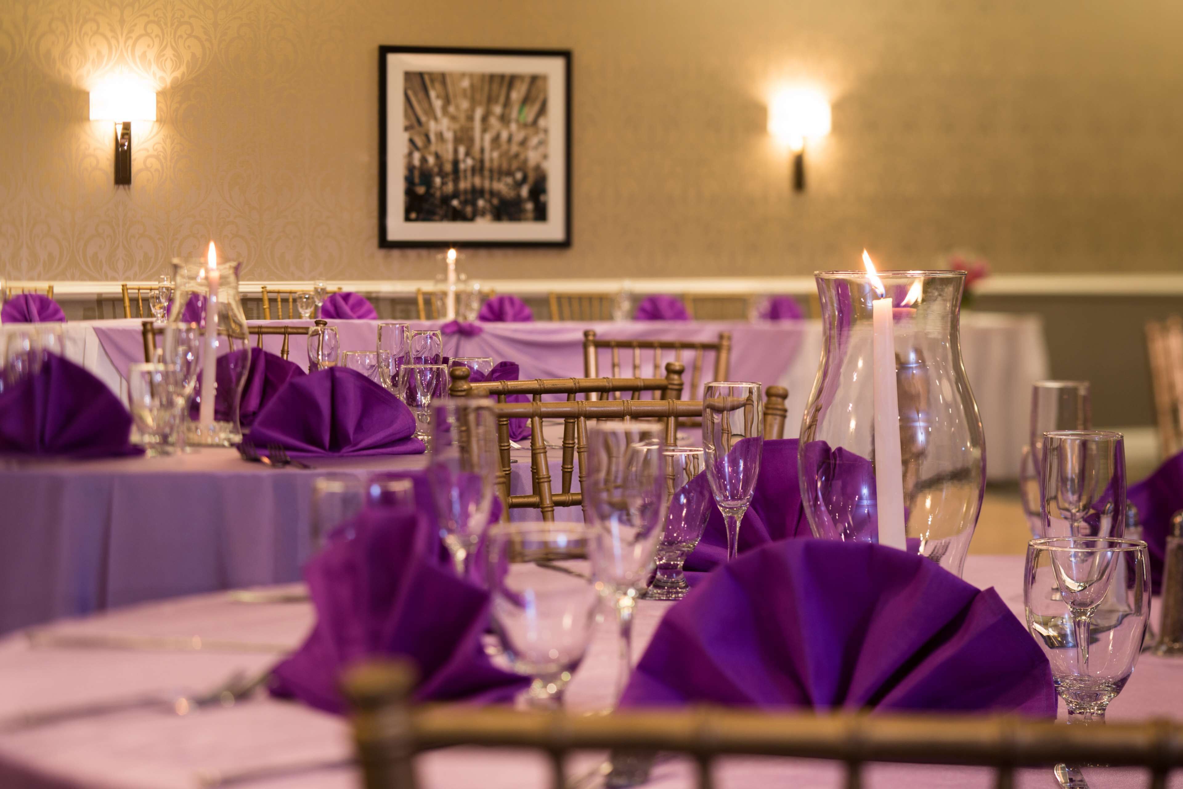 A banquet table set with purple napkins, clear glassware, and lit candles.