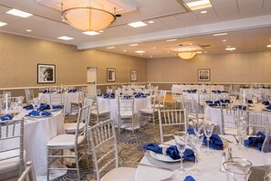 Un salón de banquetes con mesas redondas, manteles blancos y sillas de plata.