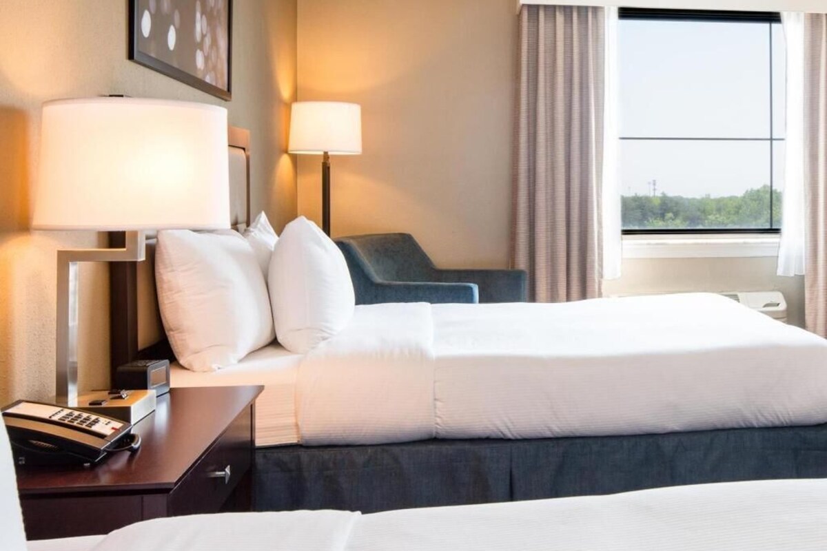 Habitación de hotel con cama, lámparas de noche, escritorio y teléfono, y vistas al exterior.