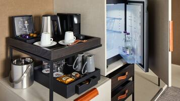 A hotel room with a minibar, a coffee maker, a kettle, and a refrigerator.