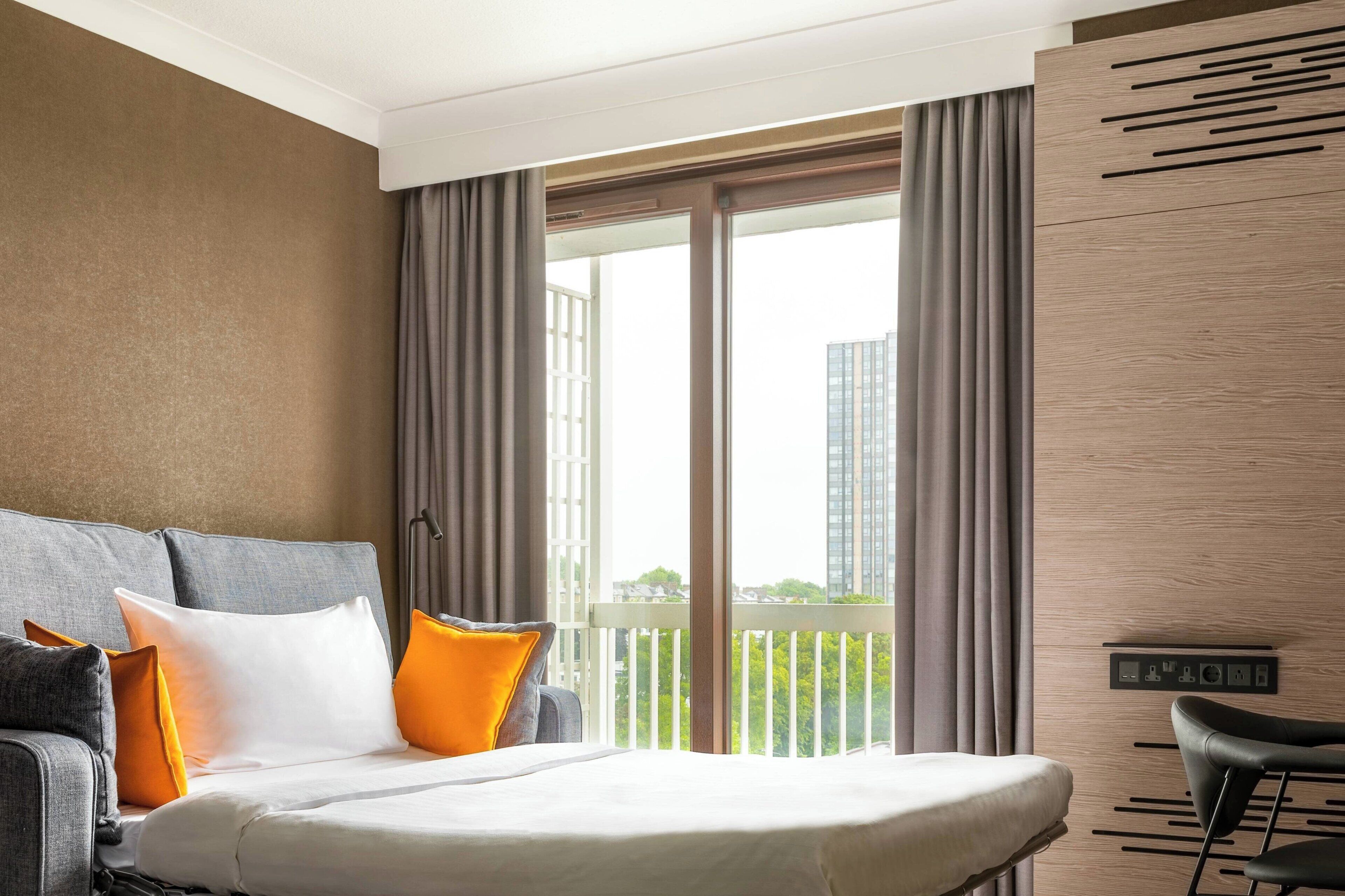 A hotel room with a large bed, a sofa, and a view of a cityscape through the window.