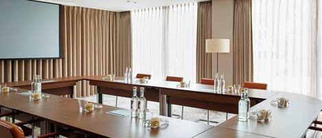 A conference room with a long table, chairs, a projector screen, and a large window with curtains.