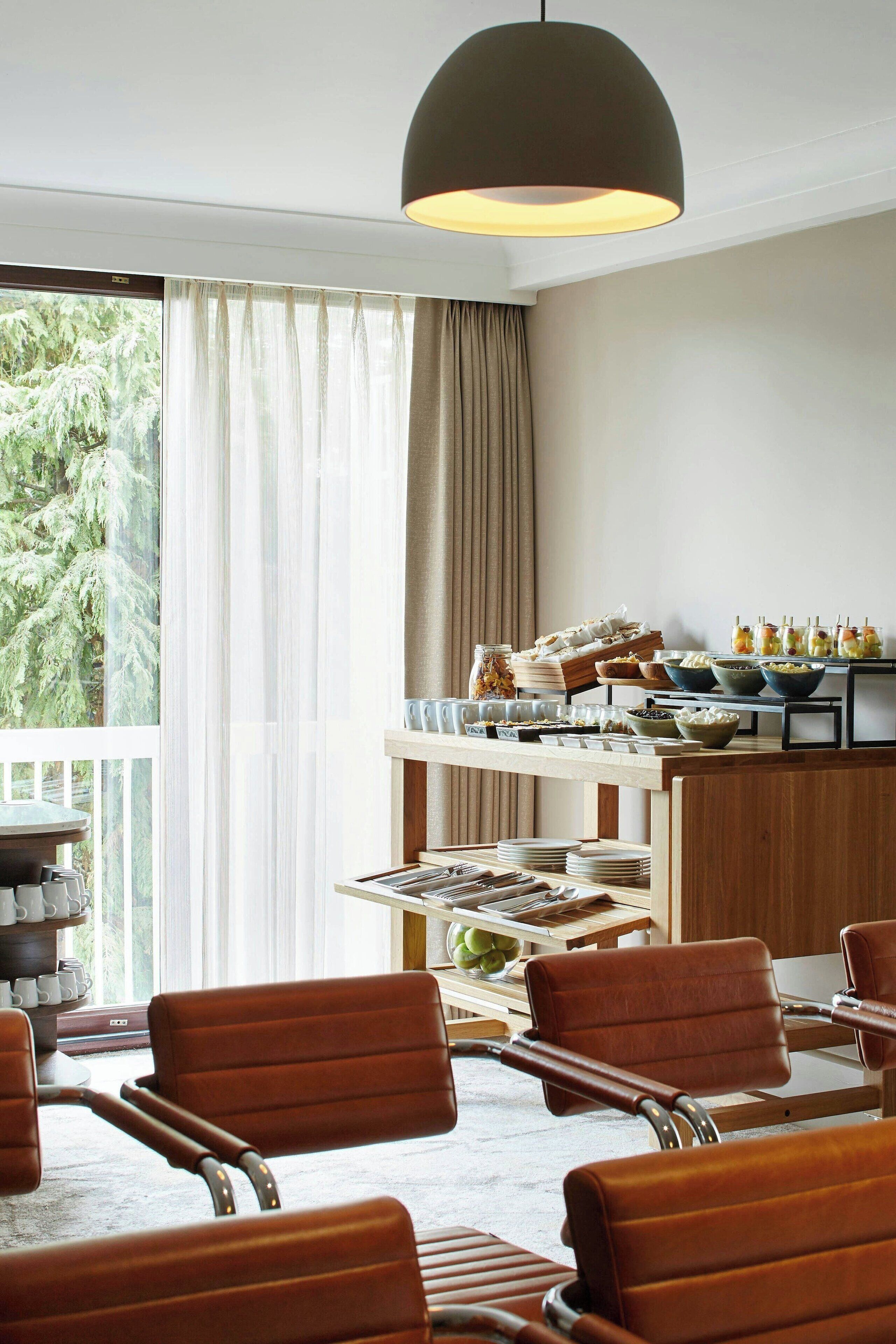 A dining area with a buffet setup, including various food items and a view of trees outside.