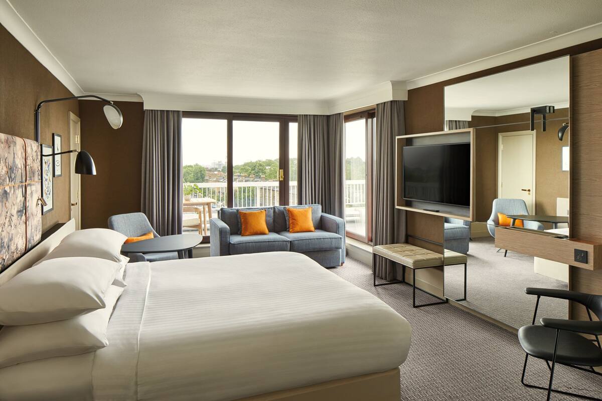 Ein Hotelzimmer mit einem großen Bett, einer Couch, einem Fernseher und einem Balkon mit Blick.