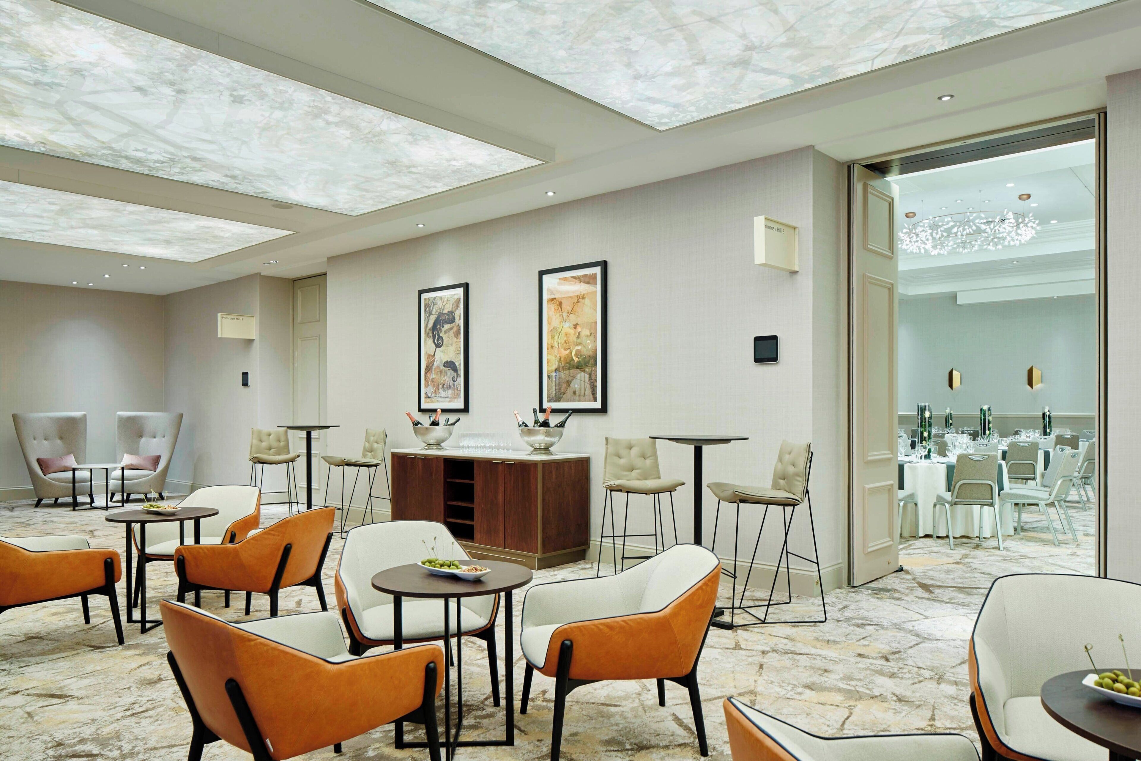 Un moderno vestíbulo de hotel con piso de mármol, varias zonas de estar y vistas hacia un comedor.
