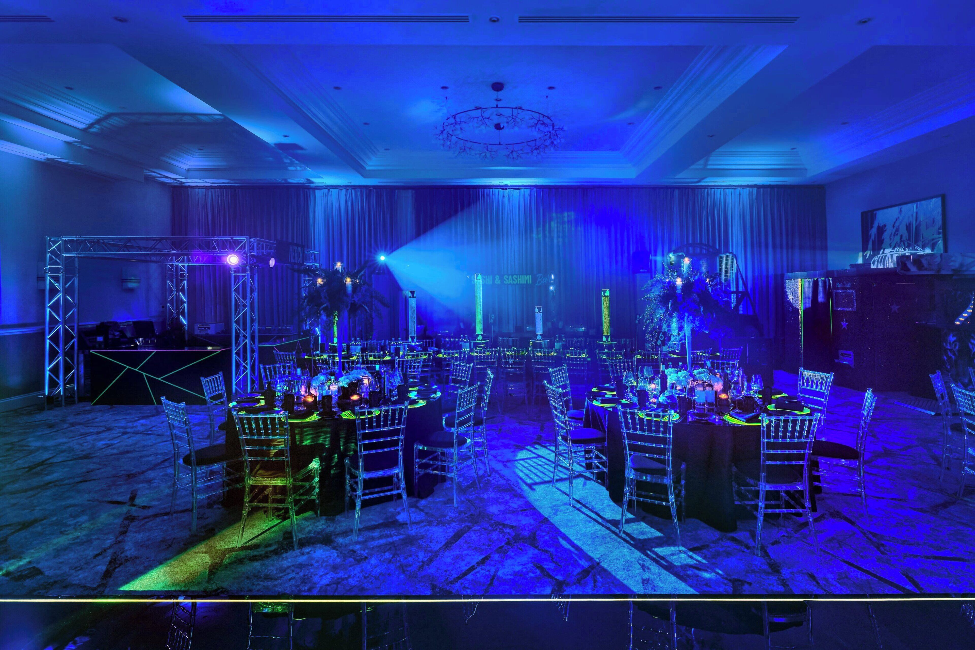 A banquet hall with tables set for a formal event, featuring a stage with a backdrop and lighting.