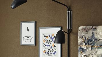 A wall-mounted desk lamp, two framed artworks, and a floral-patterned cushion.