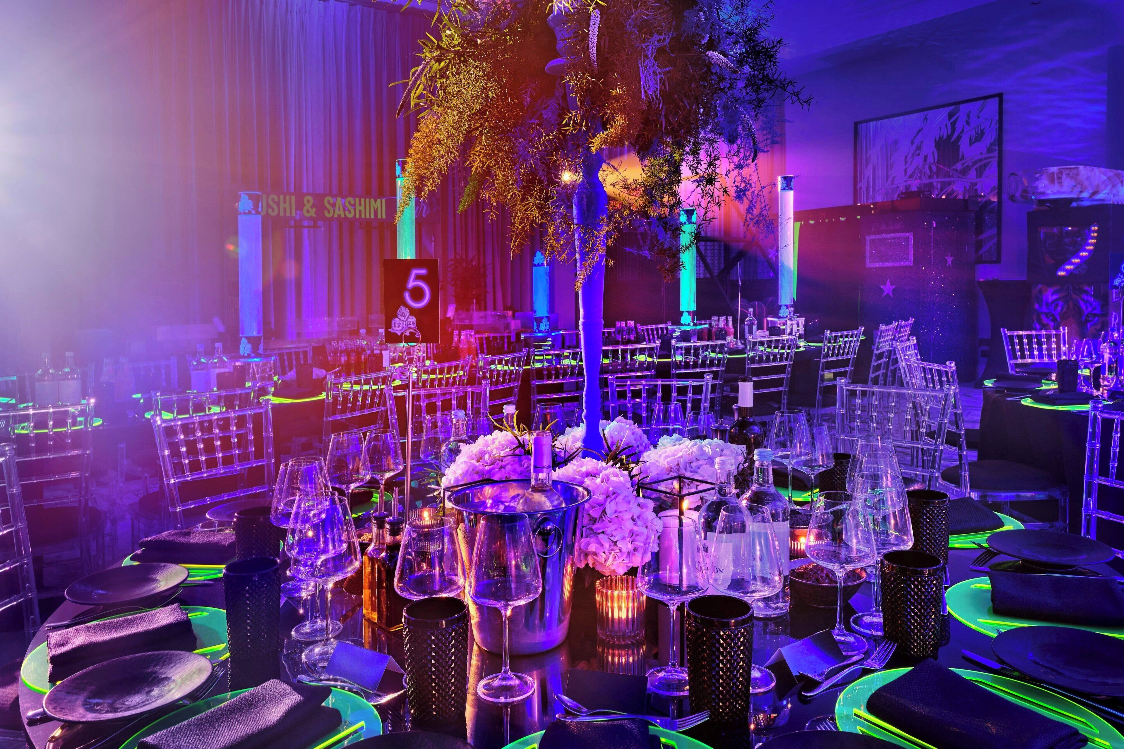 A banquet hall with tables set for a formal event, featuring floral centerpieces and illuminated by ambient lighting.
