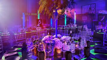 A banquet hall with tables set for a formal event, featuring floral centerpieces and illuminated by ambient lighting.