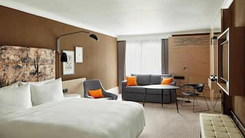 A hotel room with a large bed, a sofa, a desk, and a TV.