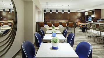 A modern hotel dining area with multiple tables and chairs, a large mirror, and a bar area in the background.